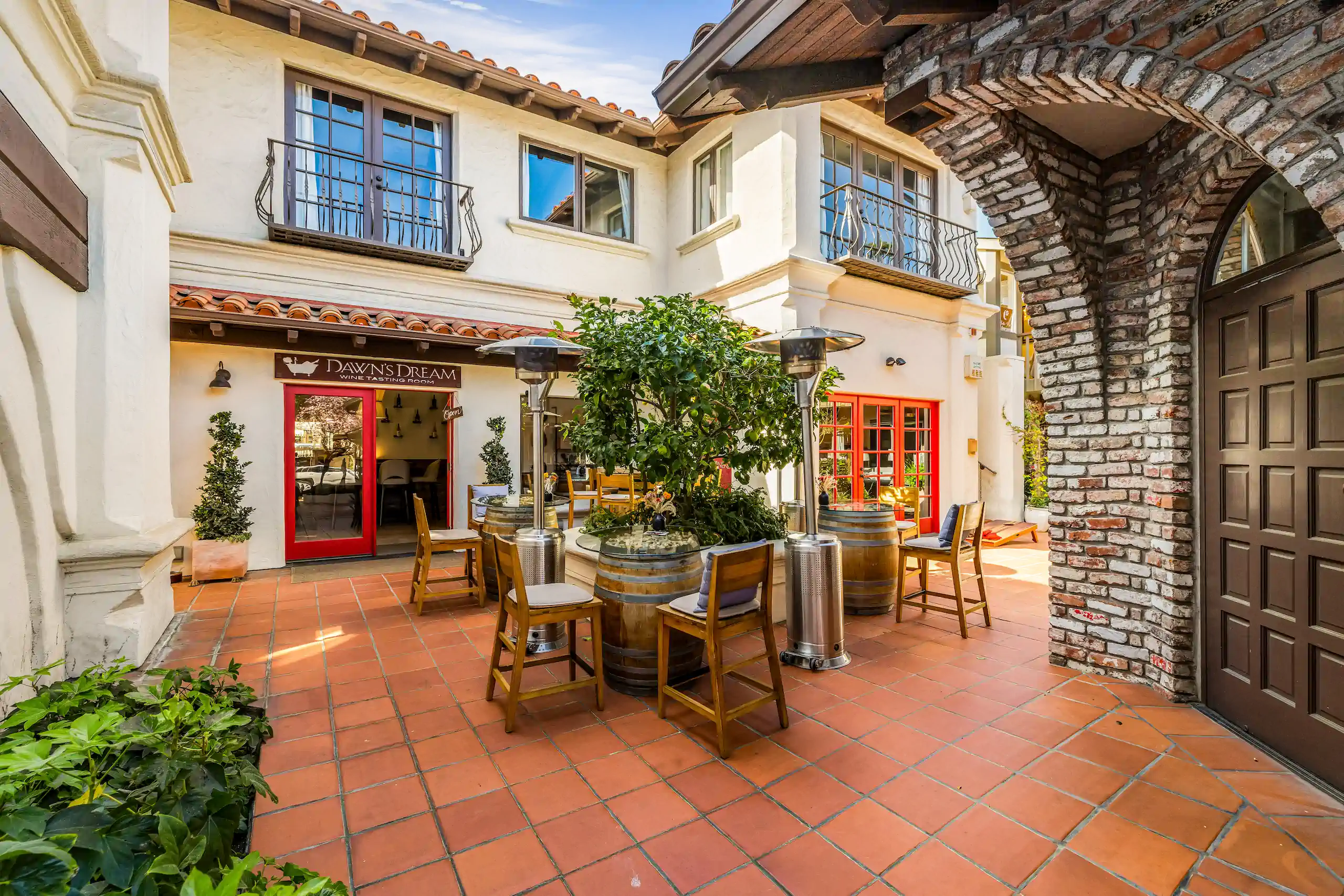 Sunny courtyard with orange tiles, tables, wooden chairs, wine barrels, and a sign reading “Dawn’s Dream.”.