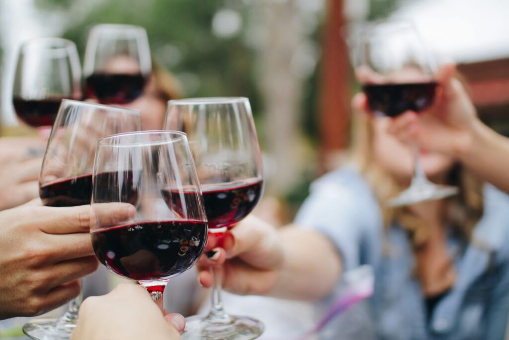 People clinking glasses of red wine together outdoors in a celebratory toast.