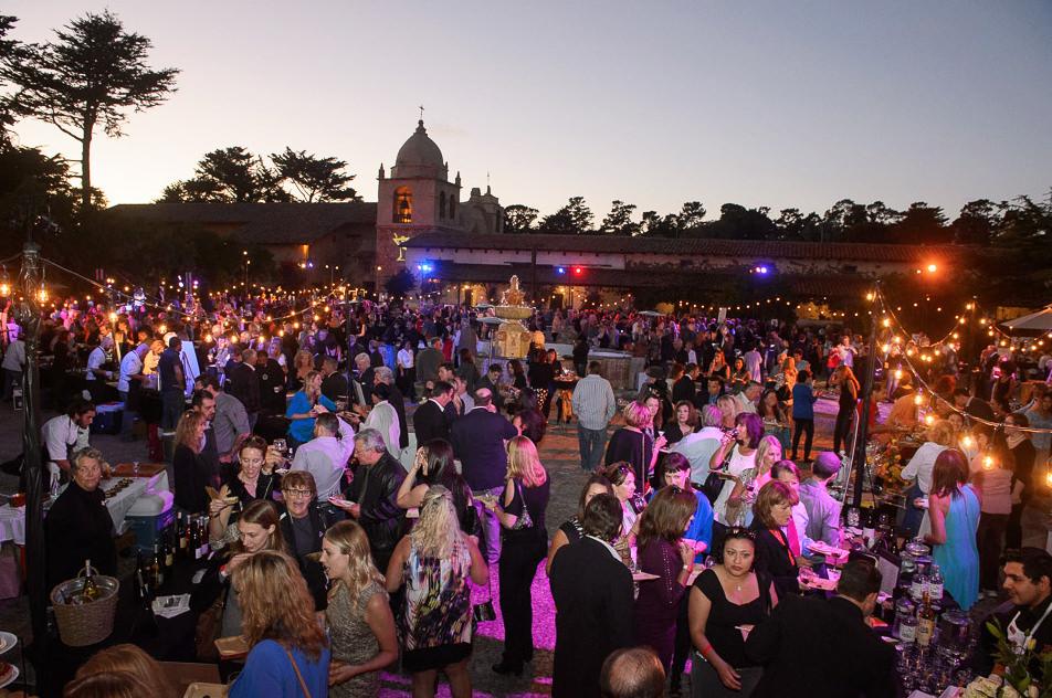 Large outdoor evening party with many people, string lights, and a historic building in the background.