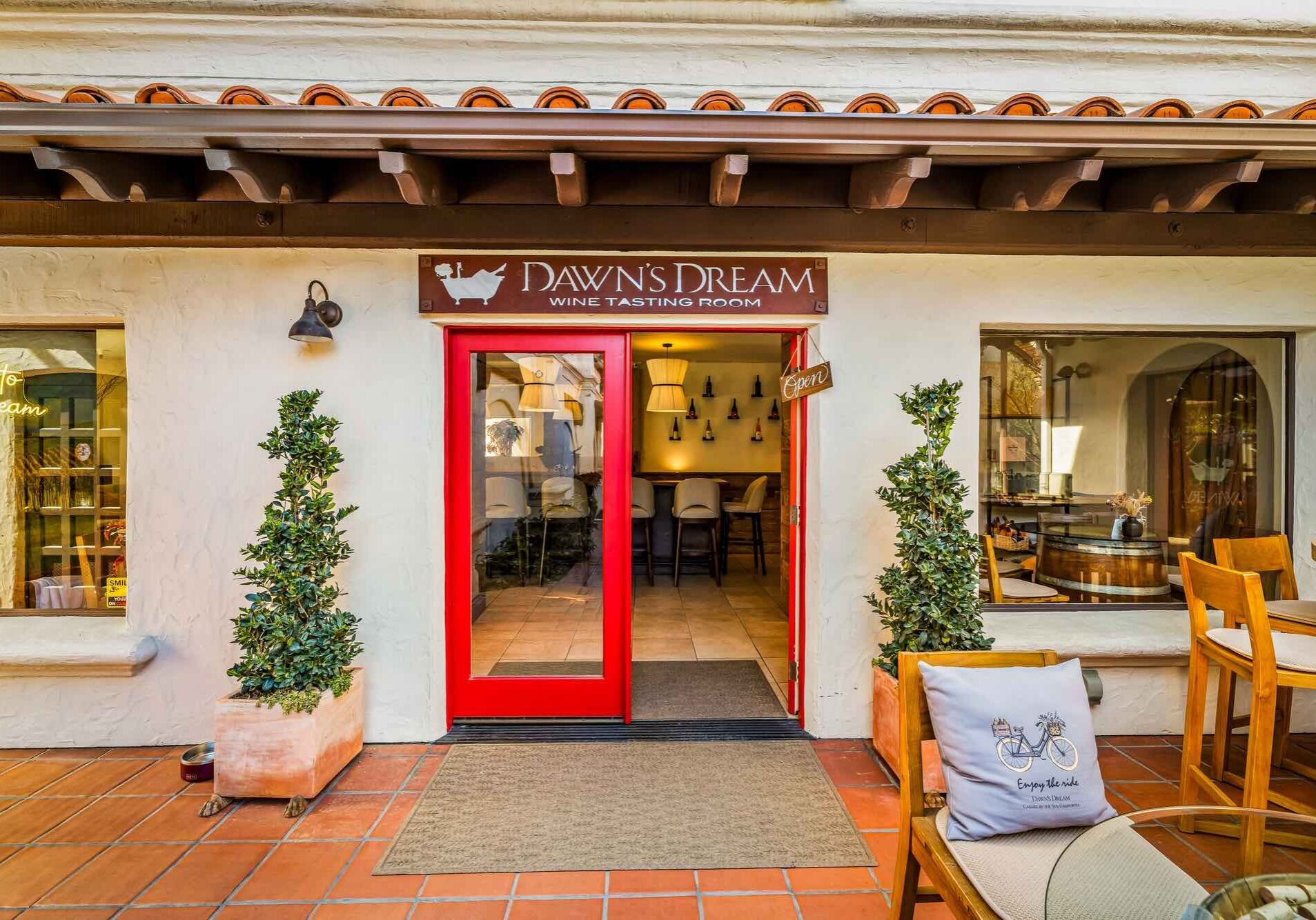 Red double doors lead into Dawns Dream wine tasting room with plants and outdoor seating on a tiled patio.