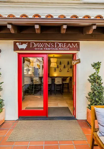 Entrance to Dawn’s Dream wine tasting room with red double doors, flanked by potted plants and patio seating.